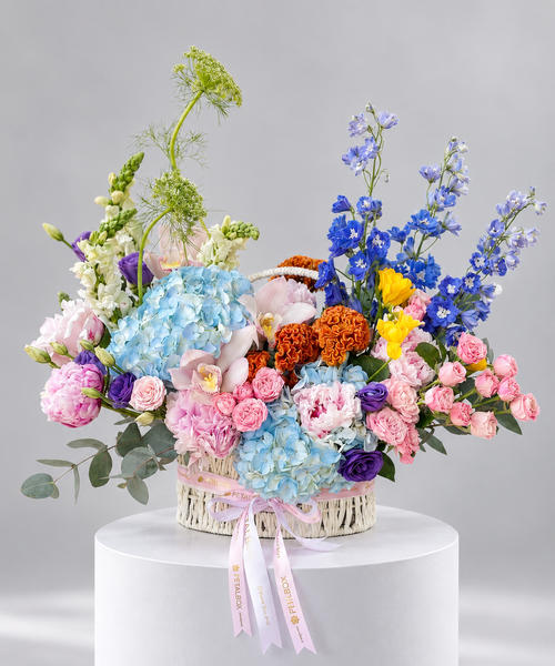 luxury garden flower hamper in a woven basket featuring blue hydrangeas, pink roses, peonies, orchids, purple flowers, yellow blooms and orange marigolds, finished with Petal Box ribbons for elegant gifting in Abu Dhabi and Dubai