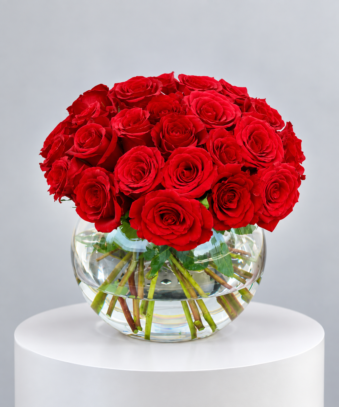 luxury red rose bouquet featuring fresh red roses arranged in a clear round glass bowl vase with visible green stems, elegant minimalist floral arrangement by Petal Box for gifting in Abu Dhabi and Dubai