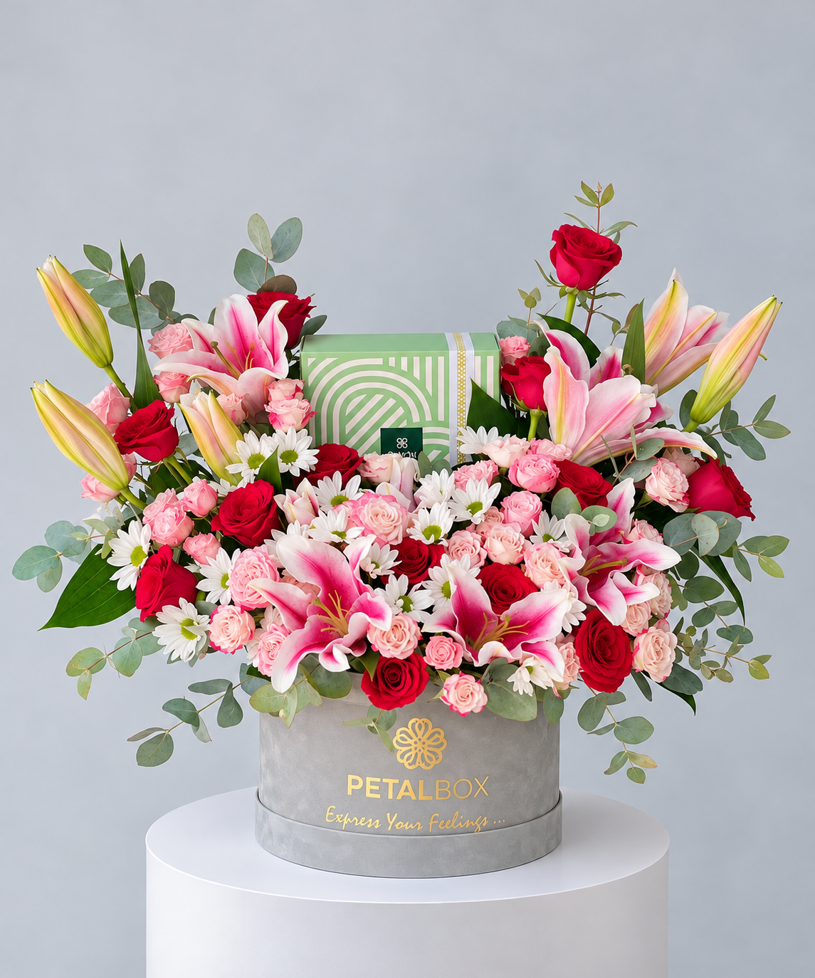 luxury floral arrangement in a grey Petal Box hatbox featuring pink lilies, red roses, blush pink roses, white daisies and eucalyptus foliage, With patchi chocolate  elegant mixed flower gift for Abu Dhabi and Dubai