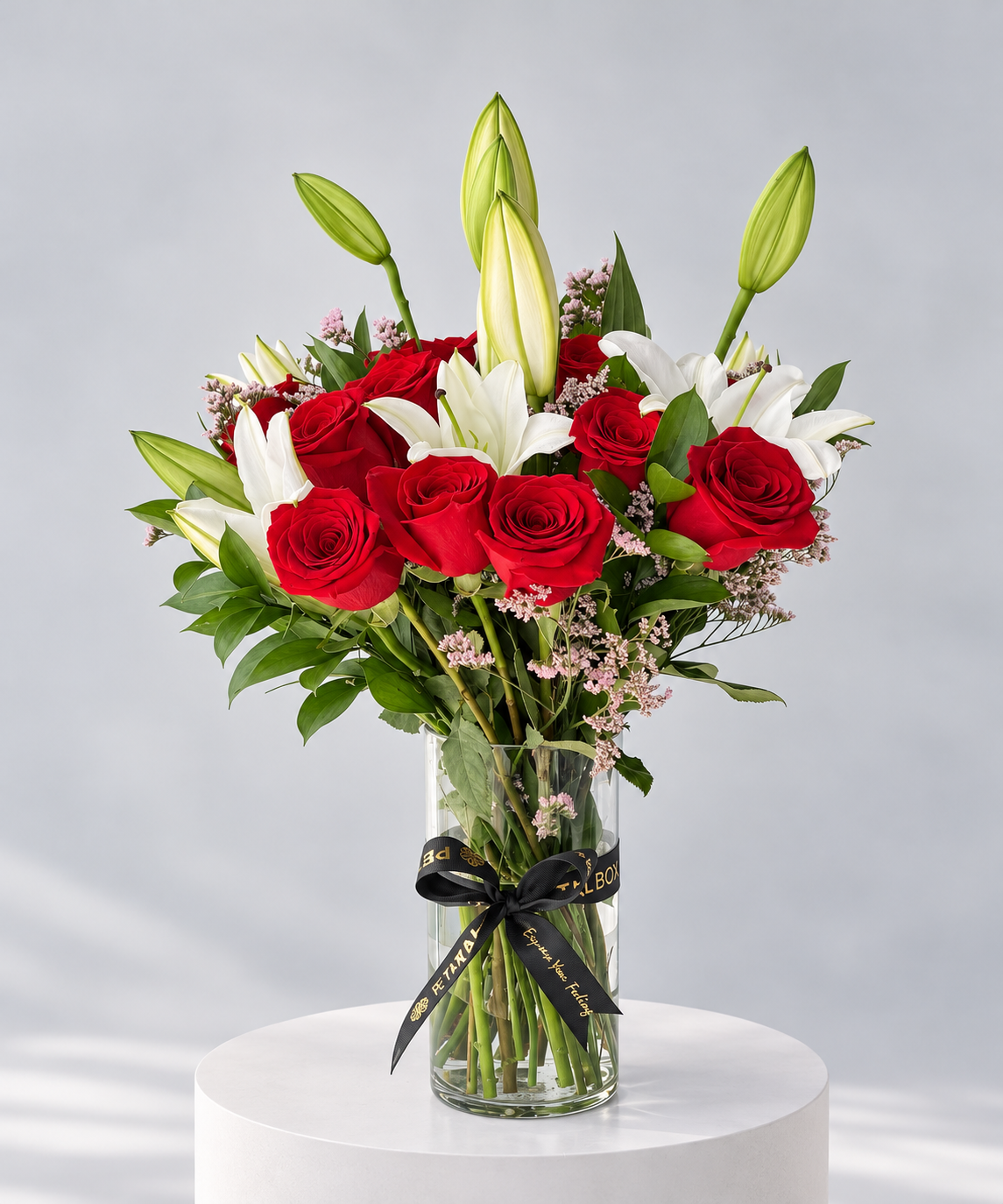 Elegant red rose and white lily bouquet arranged in a clear glass vase with a black Petal Box ribbon, featuring fresh green foliage and lily buds, ideal for romantic gifting, anniversaries and special occasions with flower delivery in Abu Dhabi and Dubai, UAE.