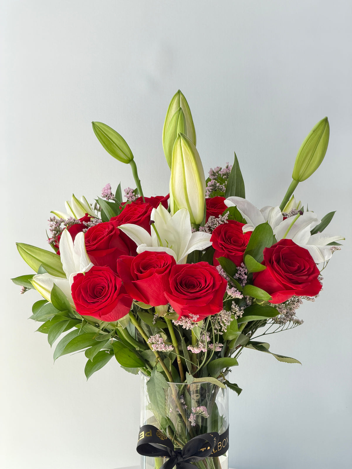 Elegant red rose and white lily bouquet arranged in a clear glass vase with a black Petal Box ribbon, featuring fresh green foliage and lily buds, ideal for romantic gifting, anniversaries and special occasions with flower delivery in Abu Dhabi and Dubai, UAE.
