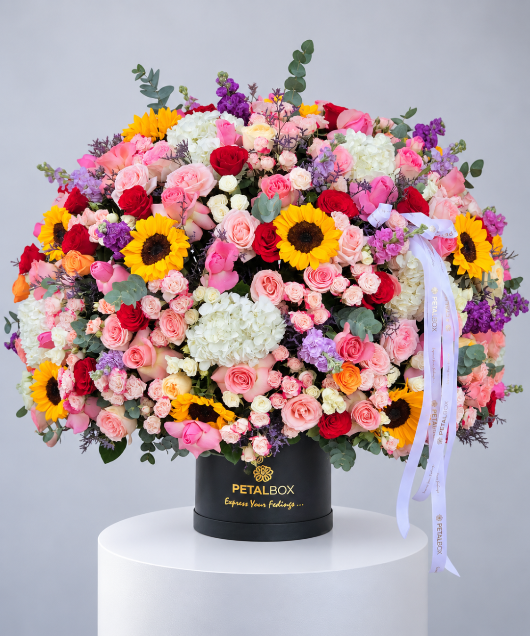 Luxury mixed flower hatbox arrangement by Petal Box featuring pink and red roses, white hydrangeas, vibrant yellow sunflowers, purple blooms and fresh eucalyptus foliage in a black hatbox with gold branding. Premium flower delivery in Abu Dhabi and Dubai, UAE, perfect for birthdays, celebrations and special occasions.