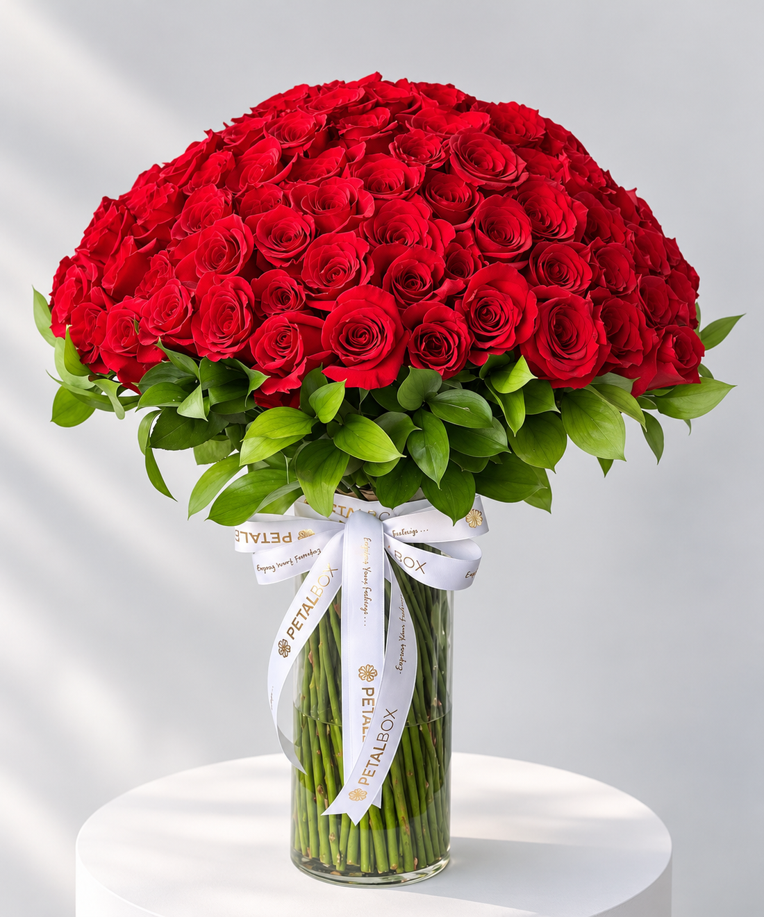 Luxury red rose dome bouquet featuring hundreds of fresh red roses and lush green foliage, elegantly arranged in a tall clear glass vase with a white and gold Petal Box ribbon, perfect for romantic gifting, anniversaries and premium flower delivery in Abu Dhabi and Dubai, UAE.