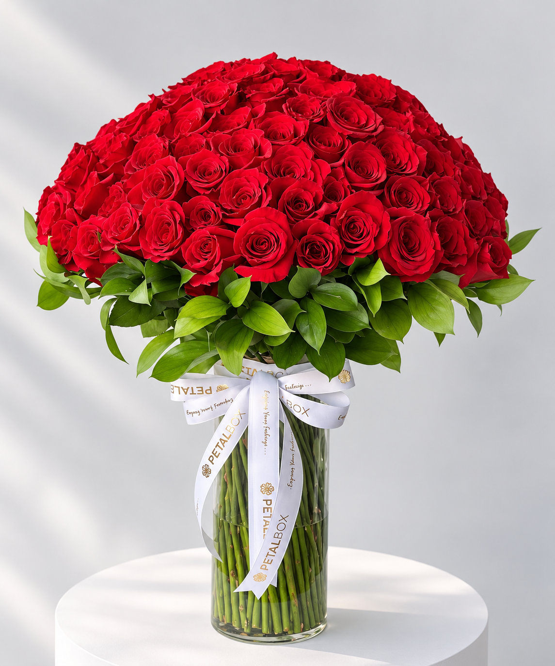 Luxury red rose dome bouquet featuring hundreds of fresh red roses and lush green foliage, elegantly arranged in a tall clear glass vase with a white and gold Petal Box ribbon, perfect for romantic gifting, anniversaries and premium flower delivery in Abu Dhabi and Dubai, UAE.