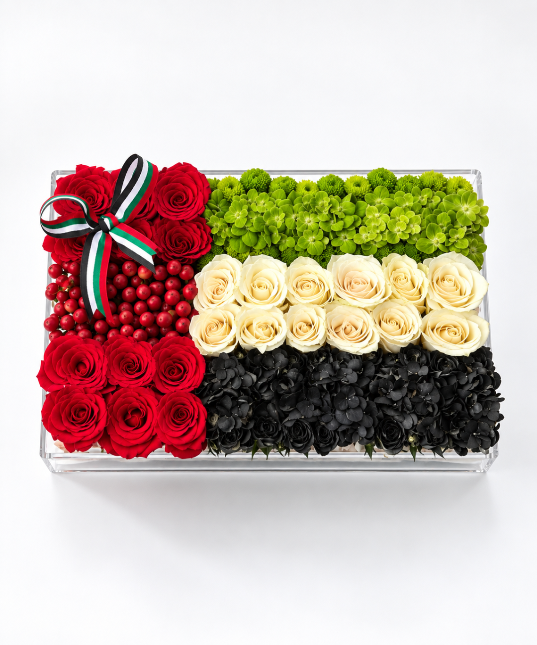 UAE flag-inspired luxury floral arrangement featuring red roses, cream roses, green chrysanthemums, red hypericum berries and black flowers in a rectangular clear box with UAE flag ribbon, perfect for UAE National Day gifting in Abu Dhabi and Dubai.
