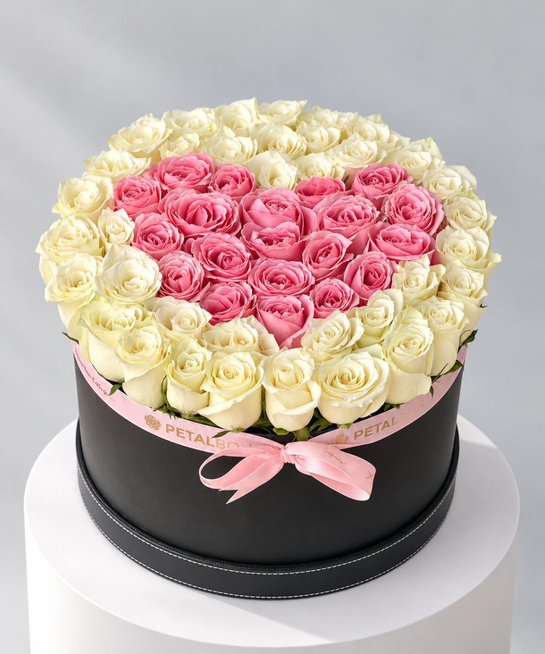 White roses around a pink rose heart in a round black hatbox with pink ribbon