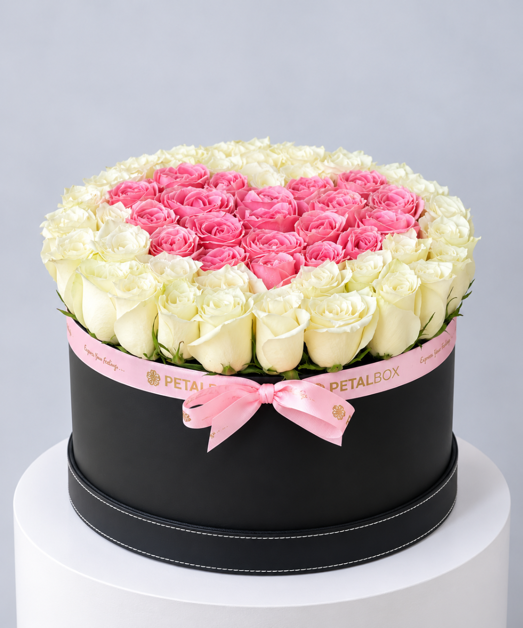 White roses around a pink rose heart in a round black hatbox with pink ribbon