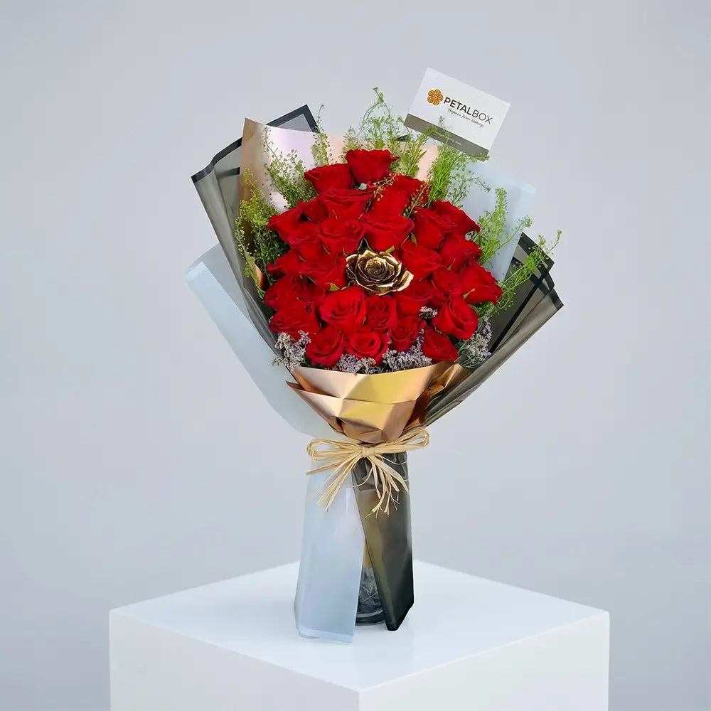 Luxury red rose bouquet with premium black and gold wrapping, featuring a golden rose centerpiece and fresh greenery for elegant romantic gifting by Petal Box UAE.