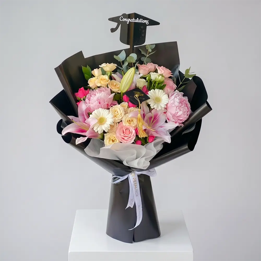 Graduation pink flower bouquet with peonies, roses, lilies and gerberas wrapped in black paper with congratulations topper