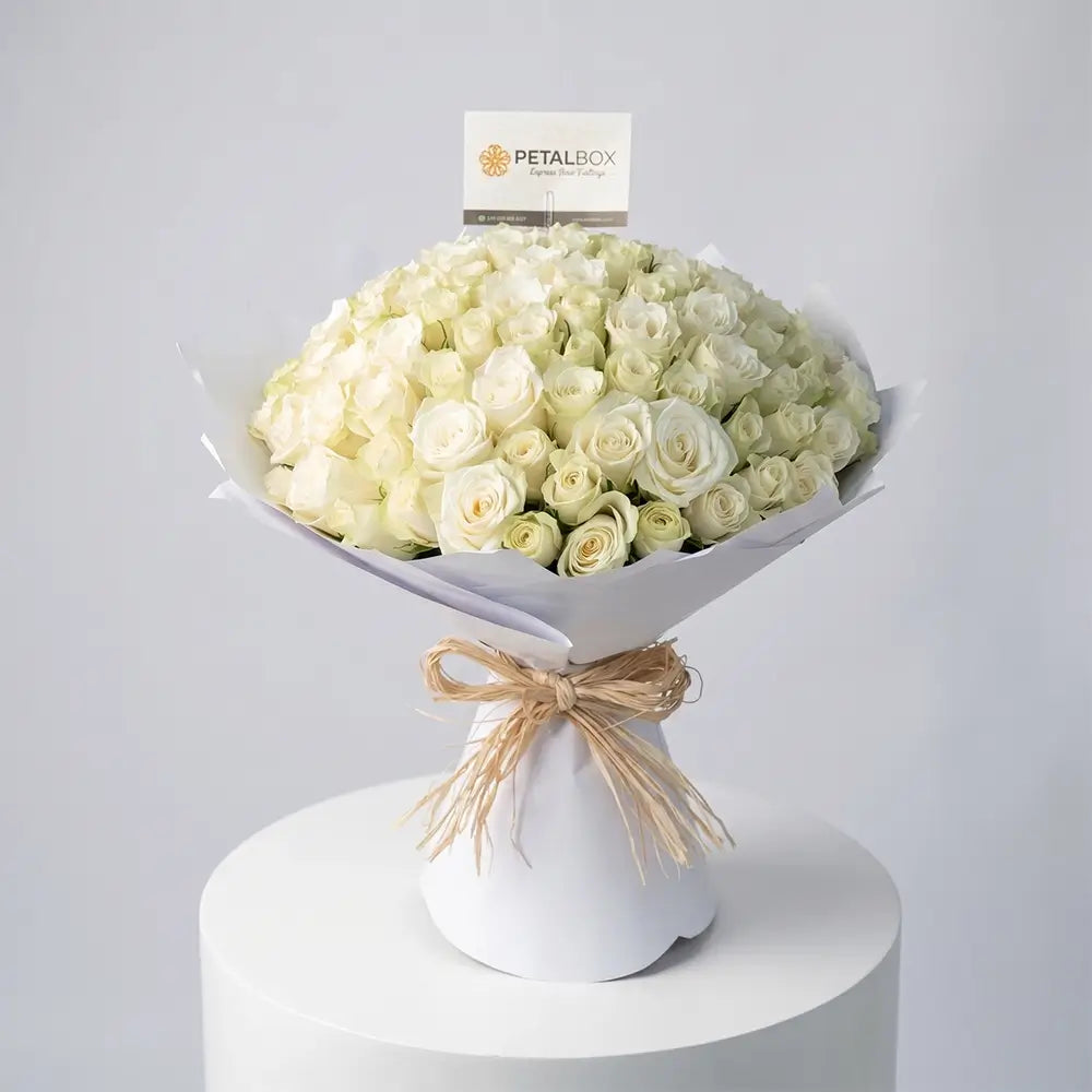 Luxury all white rose bouquet wrapped in elegant white paper with rustic raffia ribbon, featuring premium fresh roses in a timeless monochrome arrangement perfect for weddings, anniversaries, and sophisticated gifting.