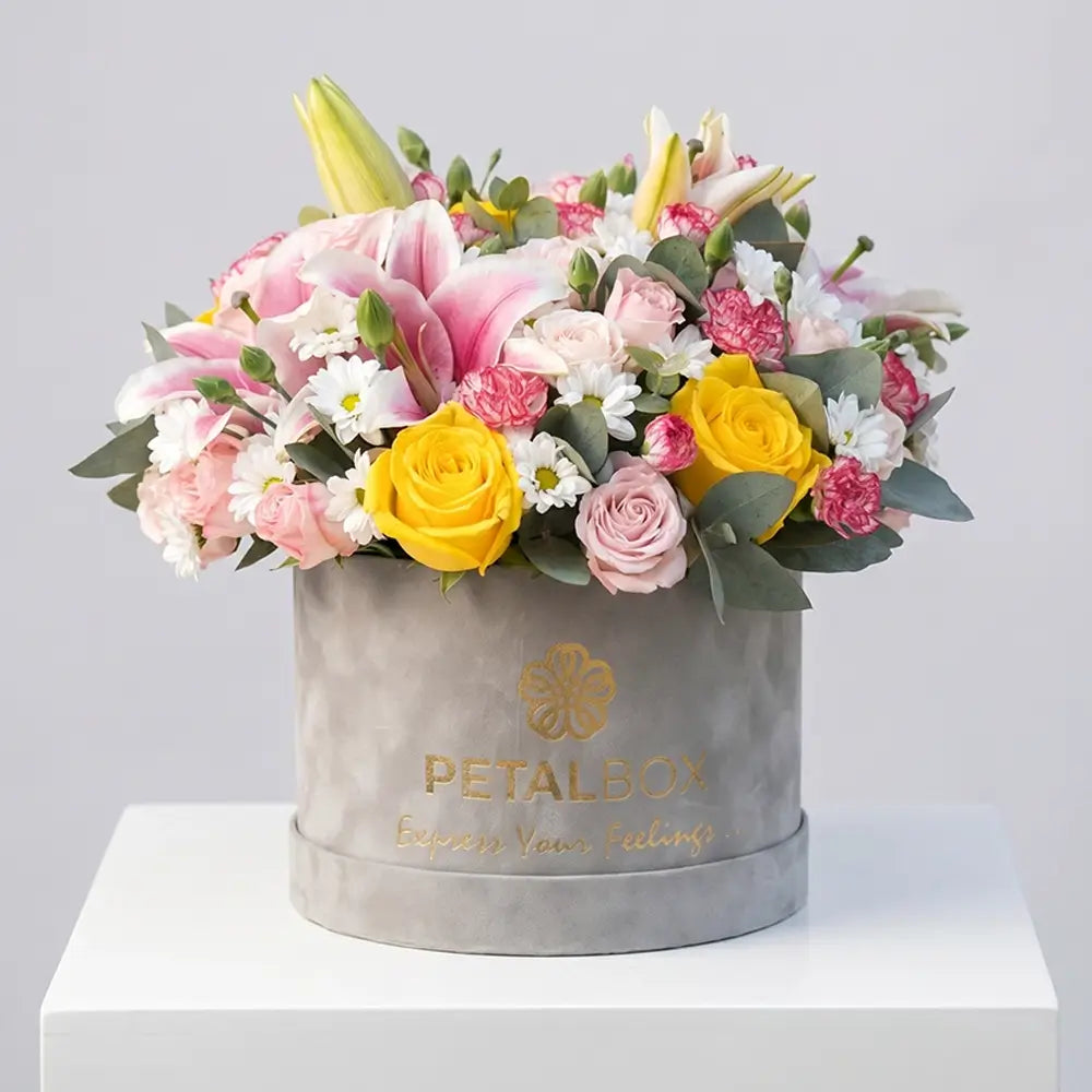 Elegant pastel flower box arrangement with pink lilies, yellow roses, blush roses, white daisies, and eucalyptus in a luxury velvet Petal Box for premium gifting and special occasions.
