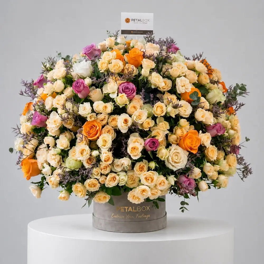 Luxury flower box arrangement with cream spray roses, orange roses, lavender roses, and fresh greenery in an elegant Petal Box floral display.
