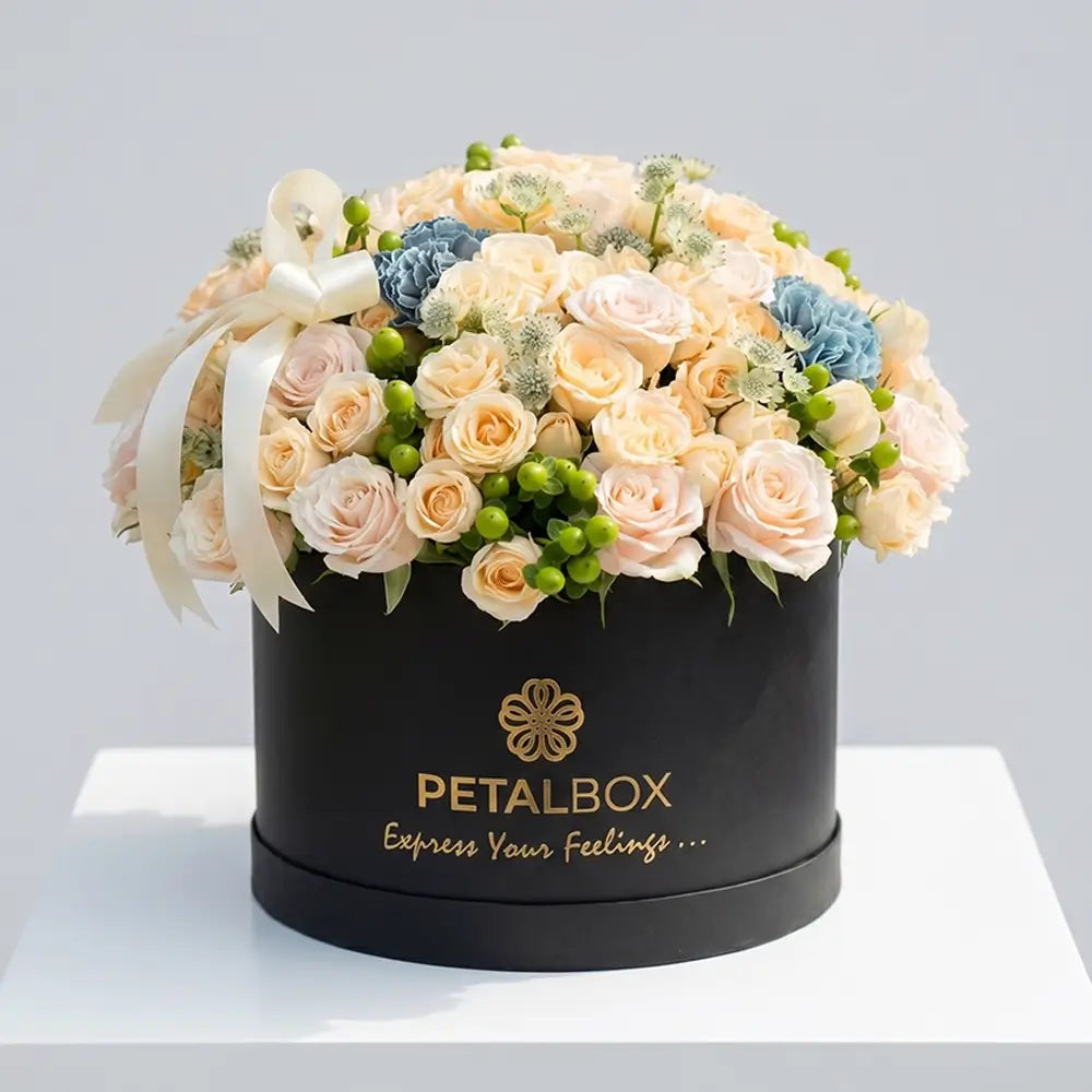 Luxury peach rose flower box arrangement with cream roses, blue carnations, green hypericum berries, and delicate seasonal flowers in a premium black Petal Box for elegant gifting in Abu Dhabi and Dubai.