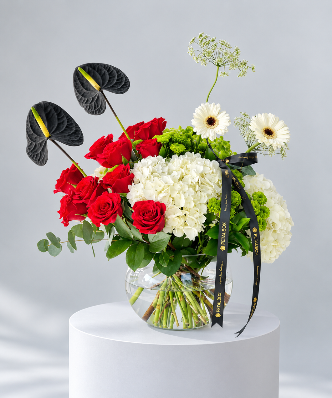 Clear glass fishbowl with red roses, white hydrangea, white gerbera and two black anthurium