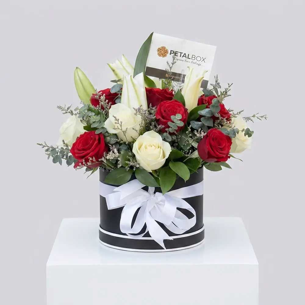 Luxury red and white rose arrangement with white lilies and eucalyptus in a black floral box with white ribbon by Petal Box.