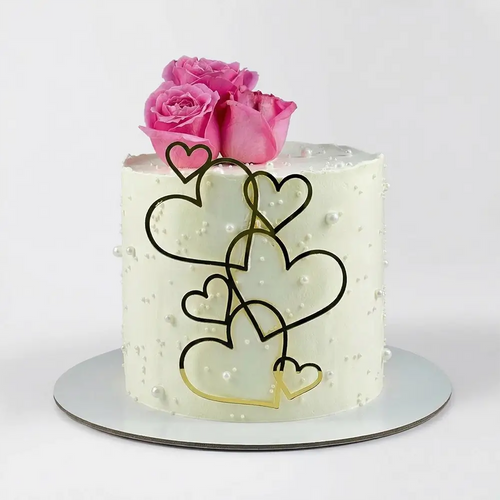 Minimal white cake with cascading gold heart outlines, fresh pink roses on top and pearl dot texture