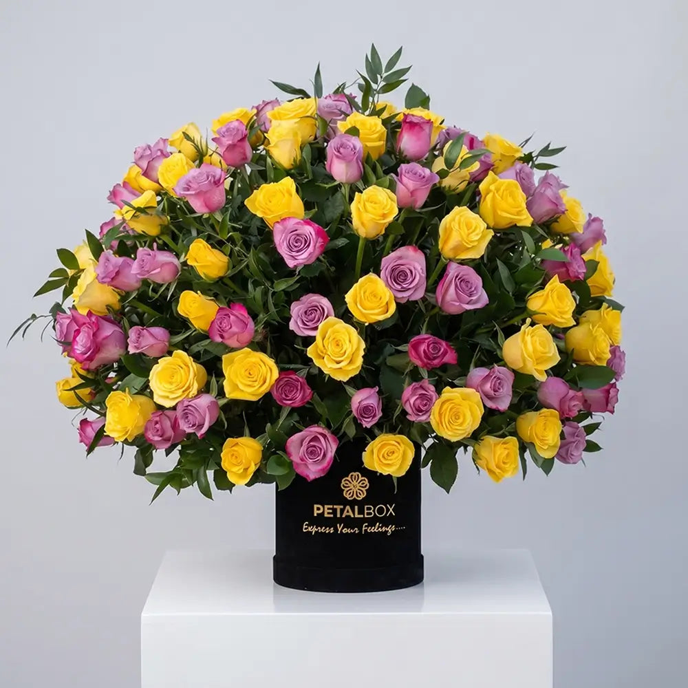 Luxury yellow and lavender rose arrangement in a black Petal Box flower box with fresh greenery, styled in an elegant premium floral display.