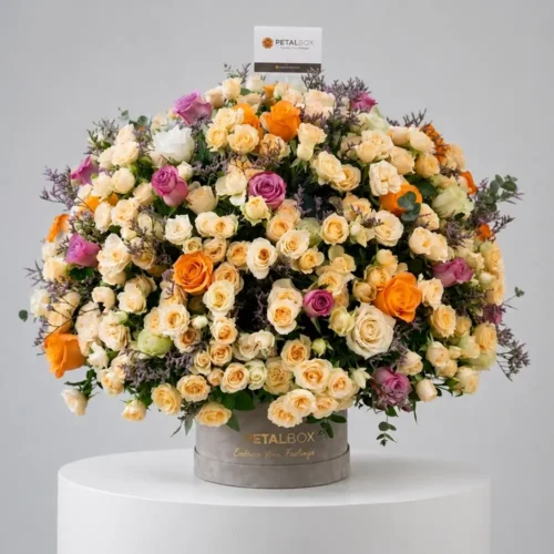 Luxury flower box arrangement with cream spray roses, orange roses, lavender roses, and fresh greenery in an elegant Petal Box floral display.