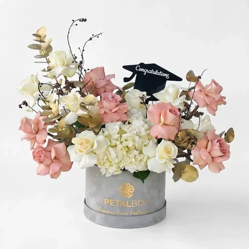 Graduation flower box with cappuccino roses, white roses, white hydrangea, gold painted eucalyptus, and green leaves in a Petal Box hatbox.