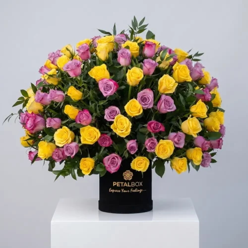 Luxury yellow and lavender rose arrangement in a black Petal Box flower box with fresh greenery, styled in an elegant premium floral display.
