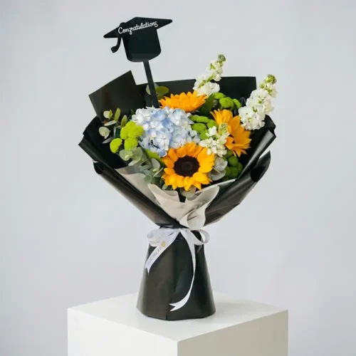 Graduation flower bouquet with sunflowers, blue hydrangea, green chrysanthemum, and white matthiola in black wrapping with white ribbon and Congratulations topper by Petal Box UAE