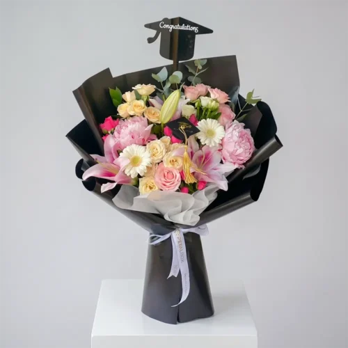 Graduation pink flower bouquet with peonies, roses, lilies and gerberas wrapped in black paper with congratulations topper