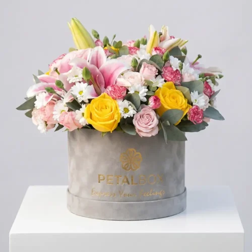 Elegant pastel flower box arrangement with pink lilies, yellow roses, blush roses, white daisies, and eucalyptus in a luxury velvet Petal Box for premium gifting and special occasions.
