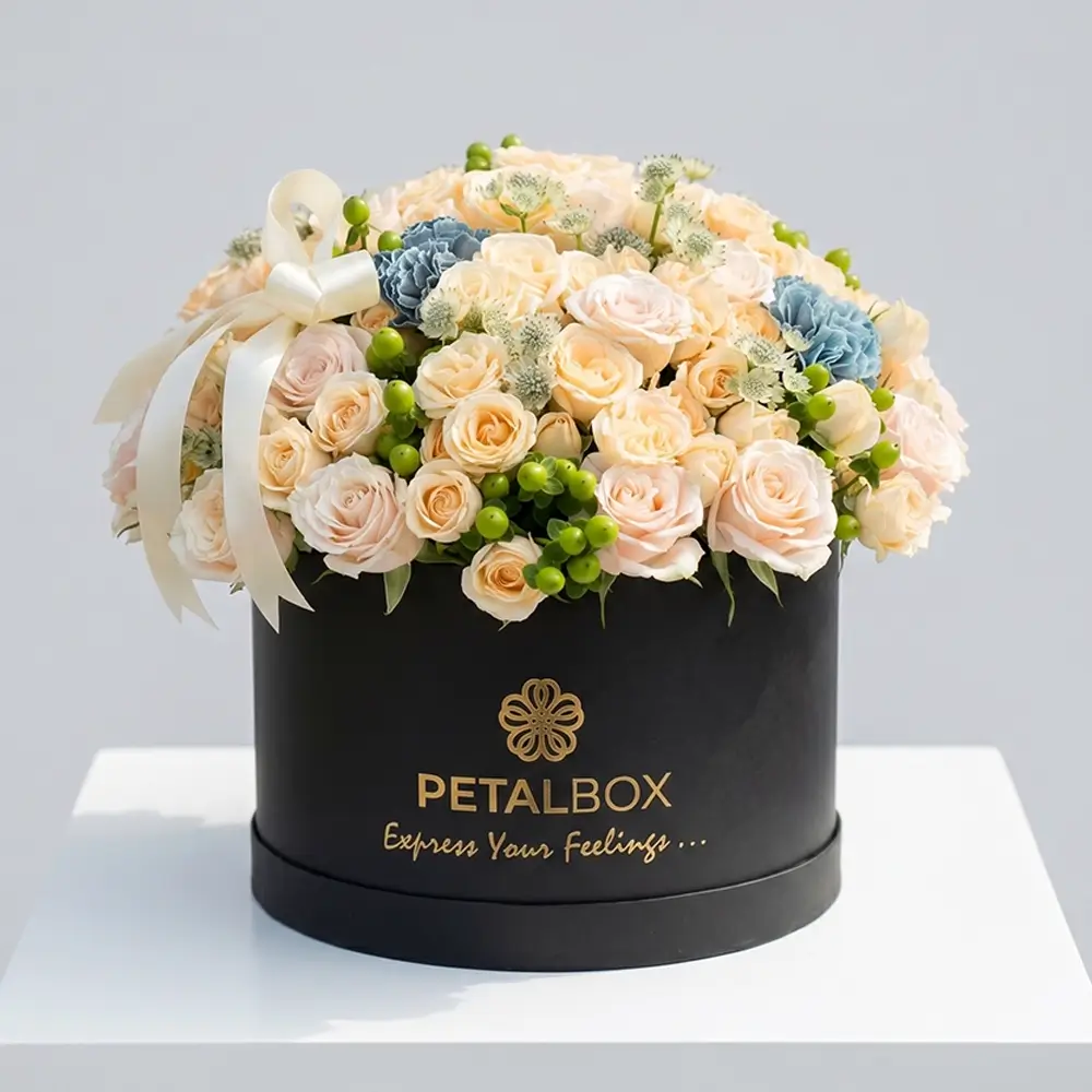 Luxury peach rose flower box arrangement with cream roses, blue carnations, green hypericum berries, and delicate seasonal flowers in a premium black Petal Box for elegant gifting in Abu Dhabi and Dubai.